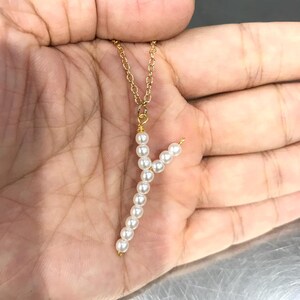 May include: A gold chain necklace with a pendant made of white pearls in the shape of the letter Y.