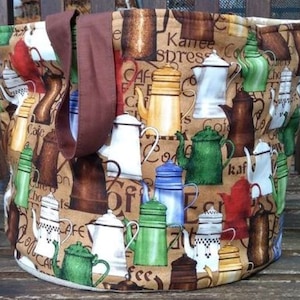 Könnte beinhalten: Eine braune Canvas-Tragetasche mit einem braunen Riemen. Die Tasche ist mit einem Muster aus Kaffeekannen und Tassen in verschiedenen Farben und Stilen verziert. Der Text "Kaffee Espresso" ist auf der Tasche sichtbar.