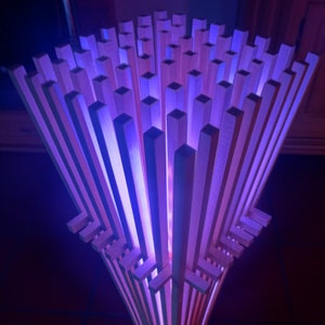 Könnte beinhalten: Eine Stehlampe aus Holz mit einem einzigartigen Design. Die Lampe besteht aus vielen dünnen Holzlatten, die in einem geometrischen Muster angeordnet sind. Die Lampe wird von innen beleuchtet und erzeugt so ein warmes Licht. Die Lampe steht auf einem gefliesten Boden.