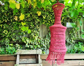 May include: A crocheted lampshade with a fringe hanging from a wooden structure covered in green ivy.