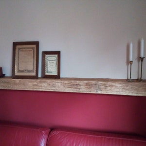 Könnte beinhalten: Ein rustikales Holzregal, das an einer weißen Wand über einer roten Wand montiert ist. Das Regal ist mit zwei gerahmten Zertifikaten und drei Kerzenständern mit weißen Kerzen dekoriert.