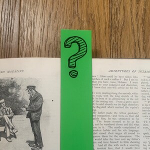 May include: A green bookmark with a question mark in black. The bookmark is placed on a page of a book with text about the adventures of Sherlock Holmes.