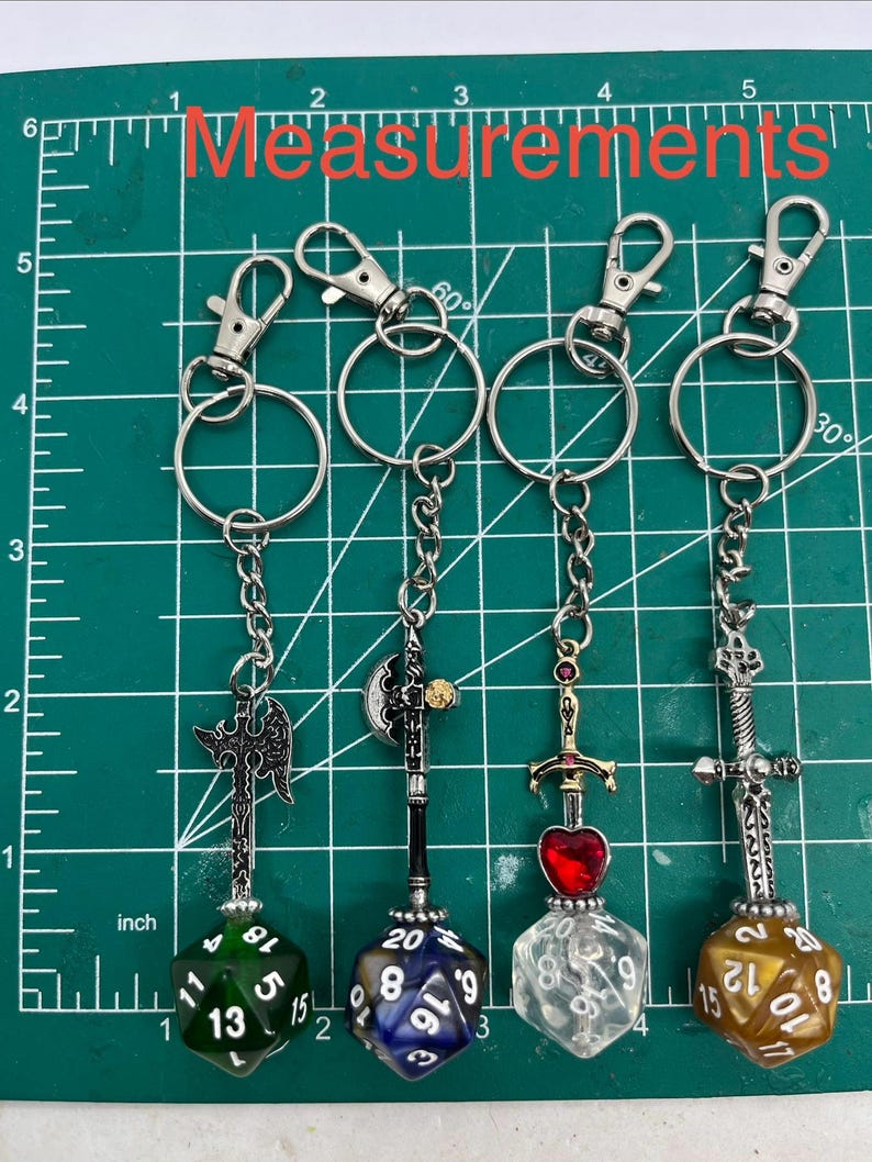 Peut inclure: Quatre porte-cl&eacute;s en m&eacute;tal avec des armes fantastiques miniatures et des d&eacute;s &agrave; vingt faces. Les armes incluent deux haches et deux &eacute;p&eacute;es, dont une avec un c&oelig;ur rouge. Les d&eacute;s sont verts, bleus, transparents et dor&eacute;s. Une r&egrave;gle indique moins de 13 cm.