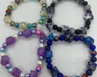 May include: Four beaded bracelets with dice-shaped beads and round beads in various colors. The bracelets feature clear, purple, blue, and black dice with gold numbering. The round beads include pearls and colorful glass beads.
