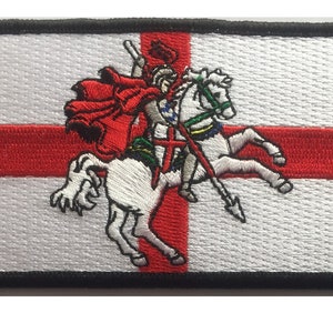 May include: Embroidered patch depicting a white horse with a red cross on its chest, ridden by a knight in red armour and a white cape. The horse is galloping to the right, and the knight is holding a spear. The patch is set against a white background with a red cross.