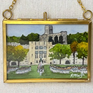 May include: A rectangular brass-framed hanging art piece featuring a watercolor painting of a large stone building with arched windows, green trees, and a group of figures in white uniforms on a lawn. The artist signature RPfaff is in the corner.