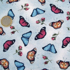 Op de afbeelding: Een blauwe stof met een herhalend patroon van kleurrijke vlinders. De vlinders zijn in verschillende tinten rood, oranje, blauw en bruin. De stof heeft een subtiele textuur.
