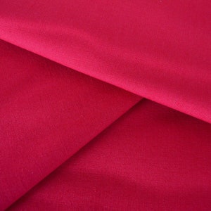 May include: Close-up of a deep red fabric with a smooth, even texture. The fabric is folded in a way that creates a triangular shape.