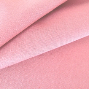 Könnte beinhalten: Nahaufnahme eines gefalteten, hellrosa Stoffes. Der Stoff hat eine subtile Textur und scheint ein weiches Material zu sein. Die Falten erzeugen Schatten und Tiefe und unterstreichen den Fall und die Textur des Stoffes. Die Gesamtfarbe ist ein zartes, gedämpftes Rosa.