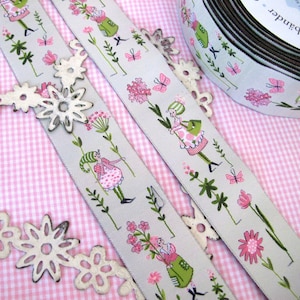 Peut inclure: Deux rouleaux de ruban gris avec un fond blanc et un motif répété de fleurs roses, de feuilles vertes, de papillons et de petites figurines. Le ruban est sur un fond vichy rose et blanc.