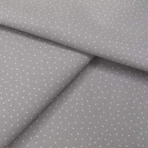 Puede incluir: Una tela de color gris claro con un patrón repetitivo de diminutos puntos blancos. El material está doblado para mostrar la textura y la distribución constante del pequeño estampado de lunares blancos sobre la superficie del tejido.