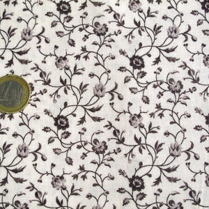 Op de afbeelding: Witte stof met een herhalend patroon van kleine zwarte bloemen en wijnstokken. De stof is textuur en heeft een subtiele glans.