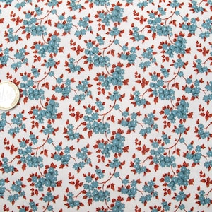 May include: A white fabric featuring a repeating pattern of small blue flowers with brown stems and leaves. A one-euro coin is placed on the left side of the fabric to provide a sense of scale for the floral print design across the textile surface.