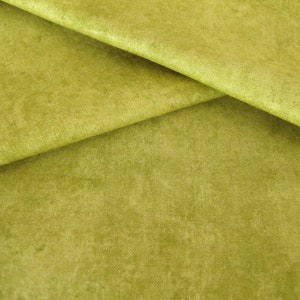 Op de afbeelding: Close-up van een getextureerde, groene stof met een subtiele glans. De stof is gevouwen op een manier die de textuur en kleurvariaties laat zien.