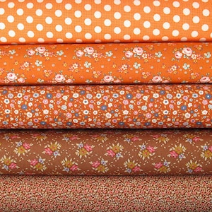 Könnte beinhalten: Vier Rollen Stoff mit verschiedenen Mustern. Die oberste Rolle ist orange mit weißen Punkten. Die zweite Rolle ist orange mit einem kleinen Blumenmuster. Die dritte Rolle ist orange mit einem kleineren Blumenmuster. Die unterste Rolle ist braun mit einem kleinen Blumenmuster.