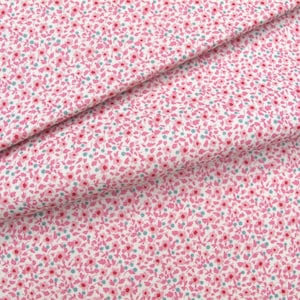 Könnte beinhalten: Ein weißer Stoff mit einem dichten, sich wiederholenden Muster aus winzigen rosa Blumen und kleinen türkisfarbenen Punkten. Das Material ist gefaltet, um die Textur und den gleichmäßigen Blumendruck auf der Oberfläche zu zeigen und das feine Design zu betonen.