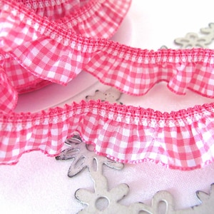 Könnte beinhalten: Rosa-weißes Gingham-Rüschenband mit weißem Hintergrund und rosa Quadraten. Das Band ist in der Mitte gefaltet und die Rüschen sind sichtbar.