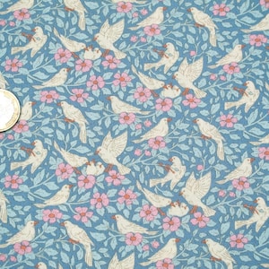 Könnte beinhalten: Ein Stoff mit einem sich wiederholenden Muster aus weißen Vögeln, rosa Blüten und hellblauen Blättern auf blauem Hintergrund. Die Vögel sind in verschiedenen Posen dargestellt, einige sitzen und andere fliegen. Die Blumen sind geclustert und die Blätter haben ein zartes Design.