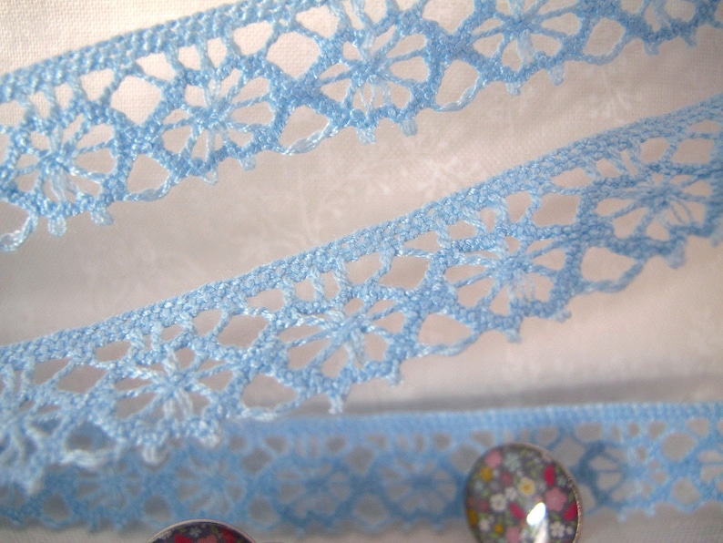 Puede incluir: Borde de encaje de crochet azul claro con un delicado patr&oacute;n floral. El encaje se muestra doblado por la mitad, con los bordes del encaje visibles.