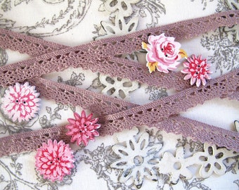 May include: A close-up of a collection of pink and white floral fabric buttons and mauve lace trim. The buttons are arranged on a white fabric background with a floral pattern.