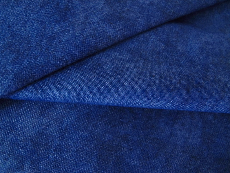 K&ouml;nnte beinhalten: Nahaufnahme eines blauen Jeansstoffs mit einer strukturierten, leicht marmorierten Oberfl&auml;che. Der Stoff ist in der Mitte gefaltet und zeigt die weiche, gewebte Textur.