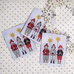 Könnte beinhalten: Drei Sätze Stoff-Geschenk-Etiketten mit Weihnachtsmotiv. Jede Etikette zeigt eine Gruppe von drei Kindern in rot, weiß und blauer Kleidung, die in einer Reihe mit einem Stern darüber stehen. Die Etiketten sind weiß mit einem grauen Punktmuster.