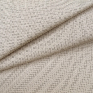 Könnte beinhalten: Ein hellbeiger Stoff mit einem dichten, sich wiederholenden Muster aus winzigen dunkelbraunen Punkten. Das Material ist diagonal gefaltet und erzeugt weiche, fließende Falten und Schatten, die die feine Textur und den Druck des Textils betonen.