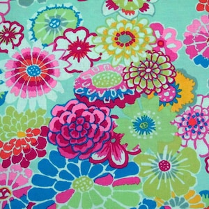 Op de afbeelding: Een kleurrijke stof met een bloemenpatroon. De stof heeft verschillende bloemen in tinten roze, blauw, groen en geel. De achtergrond is lichtblauw.