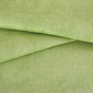 Può includere: Un primo piano di un tessuto verde chiaro con una texture sottile. Il tessuto è piegato a metà, creando un effetto di drappeggio morbido.