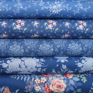 Könnte beinhalten: Ein Stapel aus fünf gefalteten Stoffballen mit verschiedenen blauen Mustern. Die Designs umfassen kleine weiße Blumenranken, rosafarbene Rosencluster, tonale blaue botanische Texturen, große weiße Blumensträuße sowie einen lebhaften Rosen- und Blattdruck.