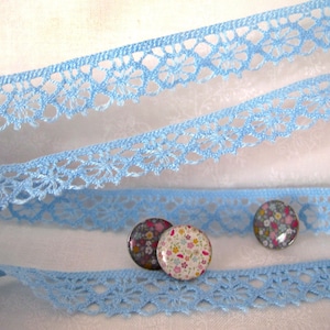 Puede incluir: Borde de encaje azul claro con un delicado patr&oacute;n floral. Tres peque&ntilde;os botones redondos con estampado floral se colocan sobre el encaje.