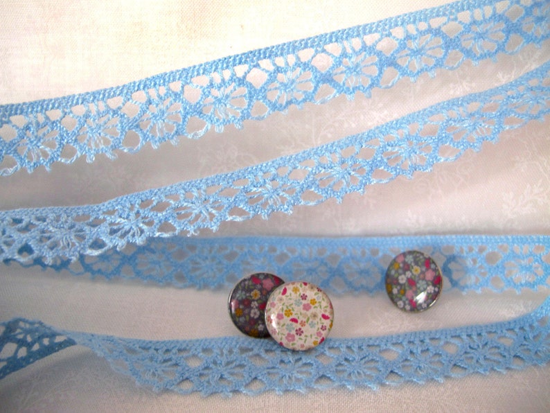 Puede incluir: Borde de encaje azul claro con un delicado patr&oacute;n floral. Tres peque&ntilde;os botones redondos con estampado floral se colocan sobre el encaje.