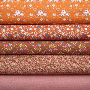 Könnte beinhalten: Fünf gestapelte Stoffrollen mit Blumenmustern. Die oberste Rolle ist orange mit rosa und weißen Blumen. Die zweite ist orange mit blauen und weißen Blüten. Die dritte ist braun mit rosa und blauen Blumen. Die vierte ist braun mit winzigen rosa Blumen. Die unterste ist einfarbig rosa.