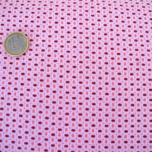Könnte beinhalten: Rosa Stoff mit einem sich wiederholenden Muster aus kleinen weißen Kreisen und größeren burgunderfarbenen Ovalen. Das Muster ist in diagonalen Reihen angeordnet.