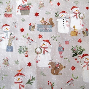 Puede incluir: Una tela beige con un patrón repetido de muñecos de nieve, ardillas, pájaros y otras ilustraciones de temática invernal. La tela presenta una variedad de colores rojo, blanco y marrón.