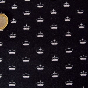 Könnte beinhalten: Schwarzer Stoff mit einem sich wiederholenden Muster aus weißen Kronen.