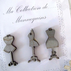 Op de afbeelding: Drie houten mannequin-versieringen met een grijze afwerking. De mannequins staan op standaards en hebben een vintage stijl. De tekst "Ma Collection de... Mannequins" staat op de witte achtergrond.
