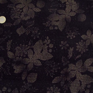 May include: Black fabric with a floral pattern. The flowers are a light grey colour and are printed on a dark background. The fabric has a textured surface.