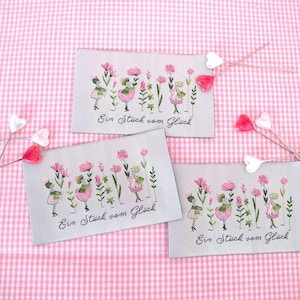 May include: Three fabric panels with embroidered images of girls in gardens. Each panel has the text "Ein Stück vom Glück" which translates to "A piece of happiness".