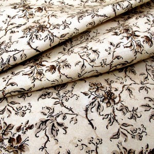 May include: Off-white fabric featuring a detailed floral design in brown and black. The fabric is folded, revealing the intricate pattern of flowers and vines. The style is vintage, ideal for crafting or home decor projects.