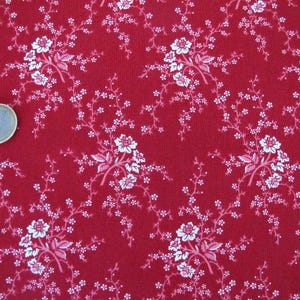 Könnte beinhalten: Roter Stoff mit weißem Blumenmuster. Der Stoff hat ein kleines, zartes Blumenmuster mit weißen Blüten und Blättern auf einem einfarbigen roten Hintergrund.