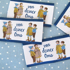Op de afbeelding: Vier witte stoffen labels met blauwe rand, elk met een kleurrijke illustratie van twee kinderen en de tekst "von deiner Oma".
