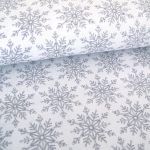 May include: White fabric featuring a repeating pattern of grey snowflakes. The snowflakes are detailed and evenly spaced, creating a winter theme. The fabric is folded, showing the texture and depth of the material, suitable for seasonal crafts.
