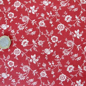 Può includere: Tessuto rosso con un motivo floreale bianco. Il tessuto presenta un piccolo motivo ripetitivo di fiori bianchi e viti su uno sfondo rosso solido.
