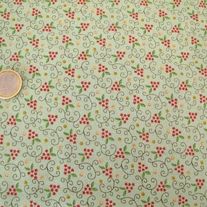 Op de afbeelding: Een groene stof met een herhalend patroon van rode bloemen, groene bladeren en bruine swirls. De stof is bedekt met een dicht patroon.