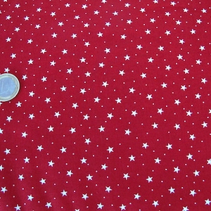 May include: Red fabric featuring a repeating pattern of white stars and small white dots. A Euro coin is placed on the fabric for scale. The fabric is suitable for sewing or craft projects.