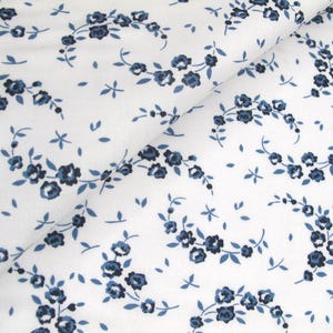 May include: White fabric featuring a repeating pattern of blue floral sprigs and small blue leaves. The flowers are clustered in small groups, creating a delicate design. The fabric is likely cotton or a similar material.