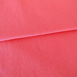 Könnte beinhalten: Nahaufnahme eines glatten, korallenfarbenen Stoffes. Der Stoff ist in der Mitte gefaltet, wodurch die Textur und Farbe sichtbar werden.