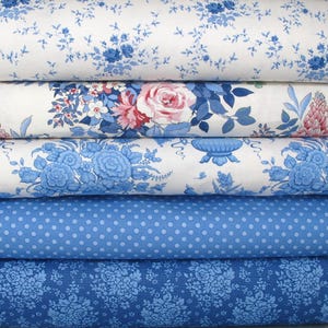 Peut inclure: Une pile de cinq rouleaux de tissu pliés présentant divers motifs. Le rouleau supérieur présente de petites fleurs bleues sur fond blanc. Le deuxième montre de grandes roses roses et un feuillage bleu. Le troisième affiche des bouquets de fleurs et des urnes bleues. Le quatrième est bleu à pois blancs. Le rouleau inférieur est bleu foncé avec un motif floral dense.