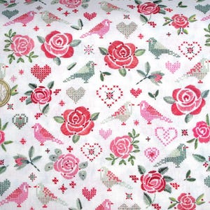 Könnte beinhalten: Weißer Stoff mit einem sich wiederholenden Muster aus rosa und roten Rosen, grünen Blättern und rosa und grünen Vögeln. Das Muster ist im Kreuzstich-Stil gestickt.